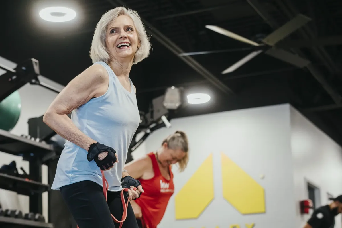 A smiling older woman working through a resistance band exercise in a small group session at Alloy Personal Training