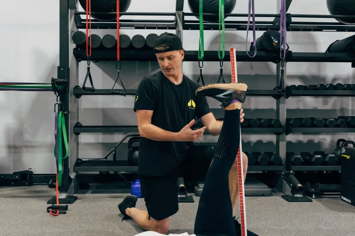 Alloy coach uses a measuring stick to assess a member's straight-leg raise during a strength assessment