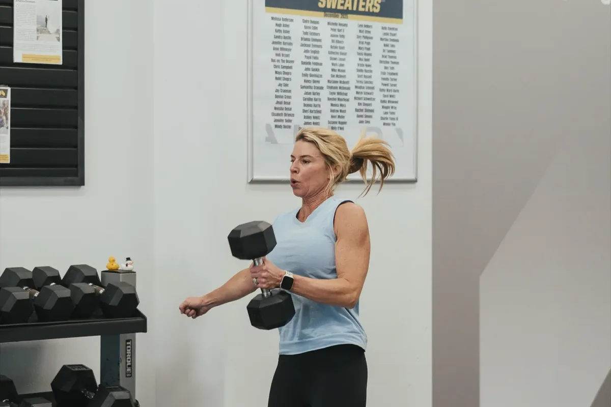 A woman works through a standing dumbbell exercise beside the rack wall at an Alloy studio