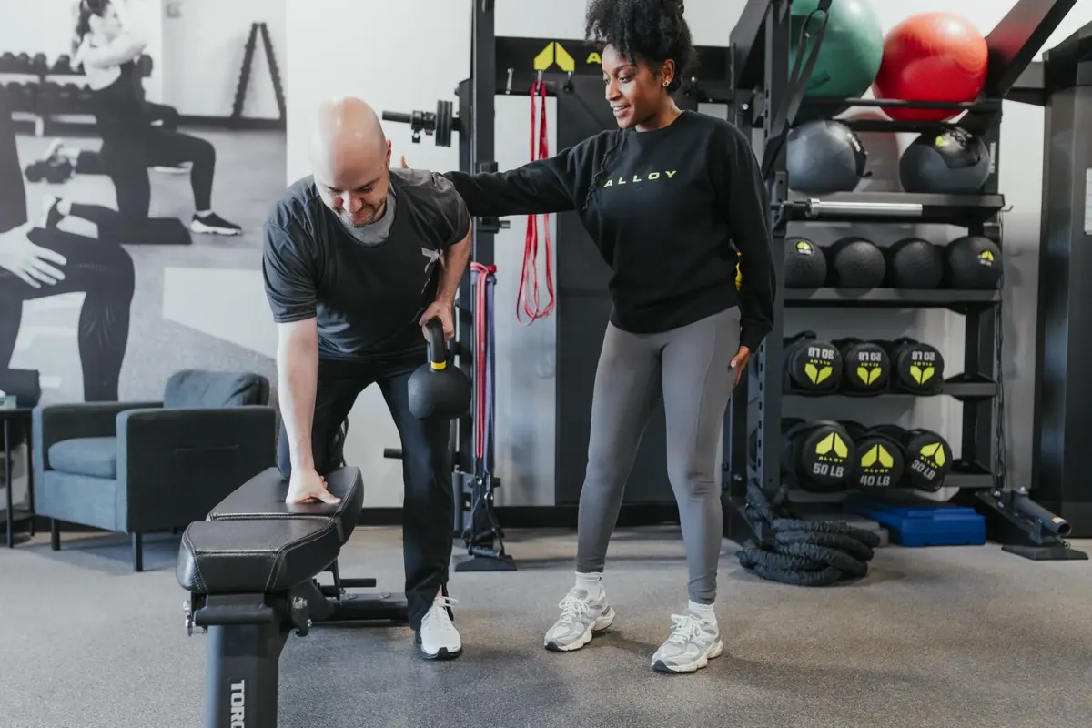 A coach guides an older member through a bench-supported kettlebell row